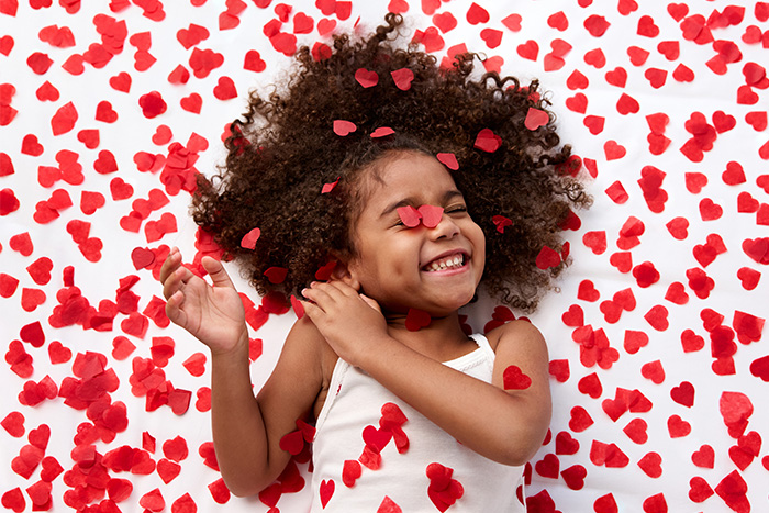 A young girl giggles while surrounded by red confetti hearts.