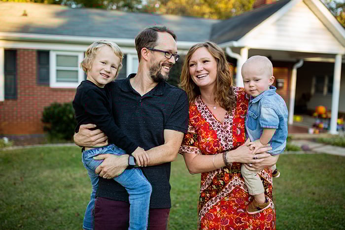 A young family celebrates in front of their new St. Cloud, MN, home, confident in their mortgage rate match guarantee.
