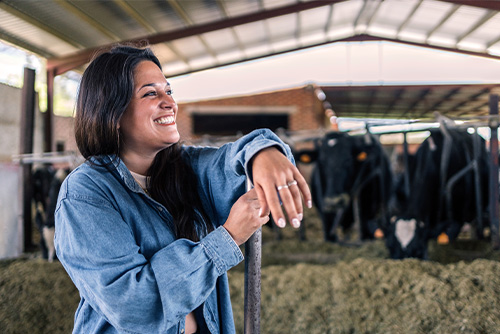 Smiling farmer with her arm resting on a pitchfork, standing in front of a row of Holstein dairy cattle near Jamestown, ND