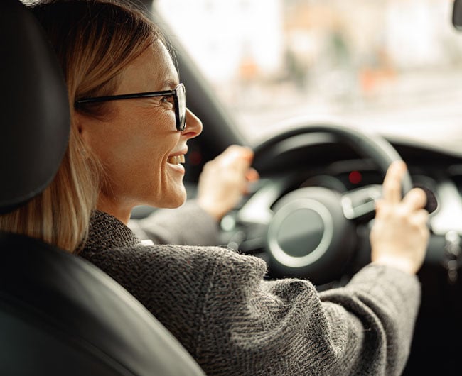 Profile of smiling woman in glasses, sitting behind the wheel of an SUV insured with the help of Gate City Insurance Agency