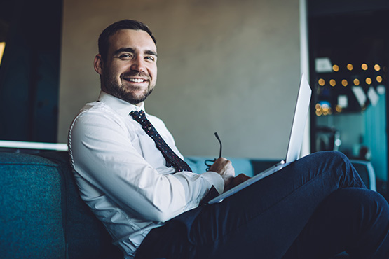Thirtysomething businessman on a blue couch, smiling after meeting with his local treasury management consultant in Fargo, ND