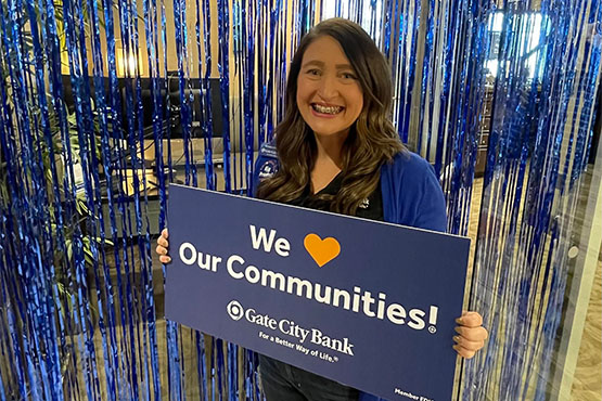 Gate City Bank’s Antoinette Sailor smiles and holds up a blue Gate City Bank sign that says “We Love Our Communities”