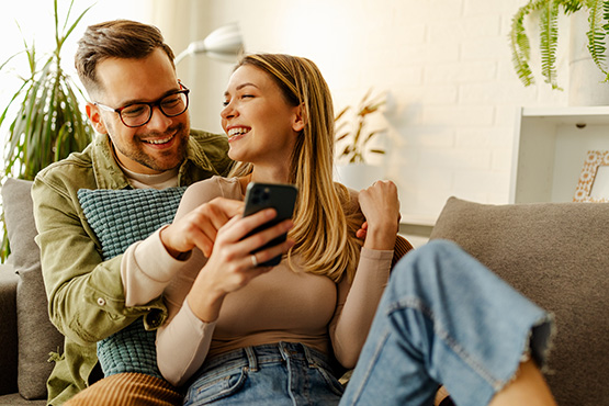 A young couple smiles as they work through their saving and budgeting plan on their mobile banking app.