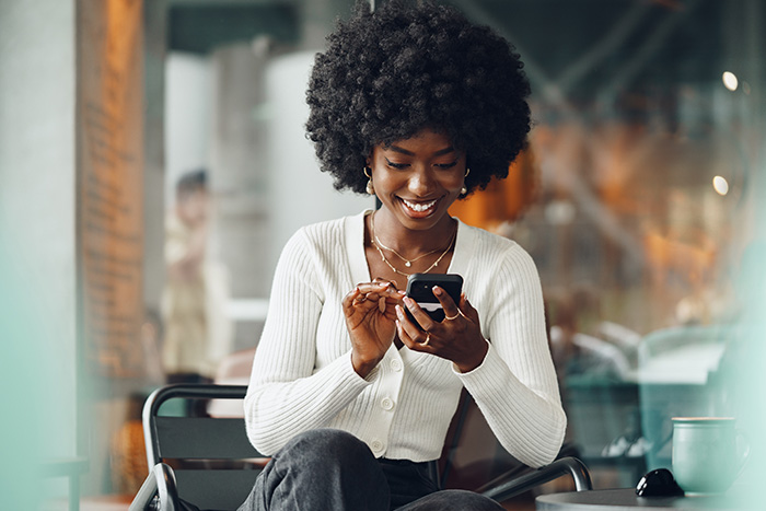 a happy woman sits down and uses her phone to navigate Gate City Bank’s upgraded online and mobile banking platform