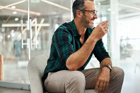 Business owner wearing a green plaid button-down shirt, relaxing with a cup of coffee in his office in downtown Fargo, ND