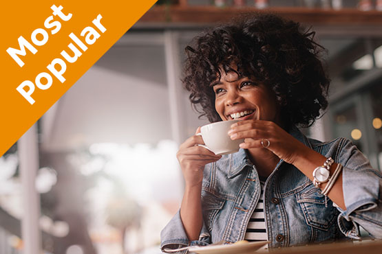 Curly-haired woman smiling and sipping coffee after opening a Benefit Interest Checking account in Bismarck, ND