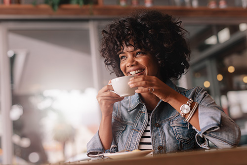 Curly-haired woman smiling and sipping coffee after opening a Benefit Interest Checking account in Bismarck, ND