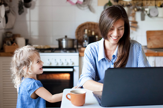 a happy mom at the kitchen table uses a laptop to secure a Gate City Bank business loan as her daughter smiles nearby