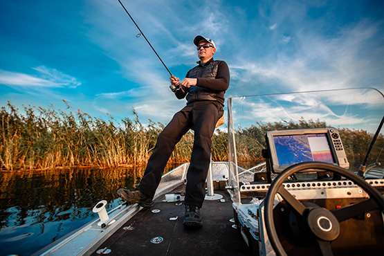 a man wearing sunglasses and a cap sits and fishes from his boat after reading about Gate City Bank’s tips for buying a boat