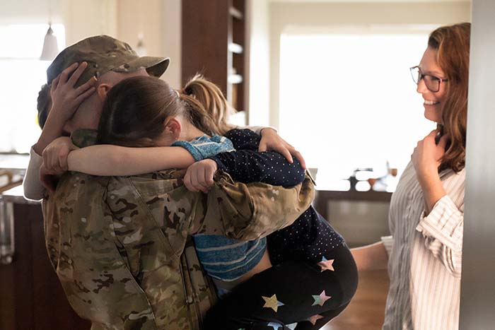 Military service member hugs his two kids, while his wife tries to hold back tears in their home purchased with a VA loan