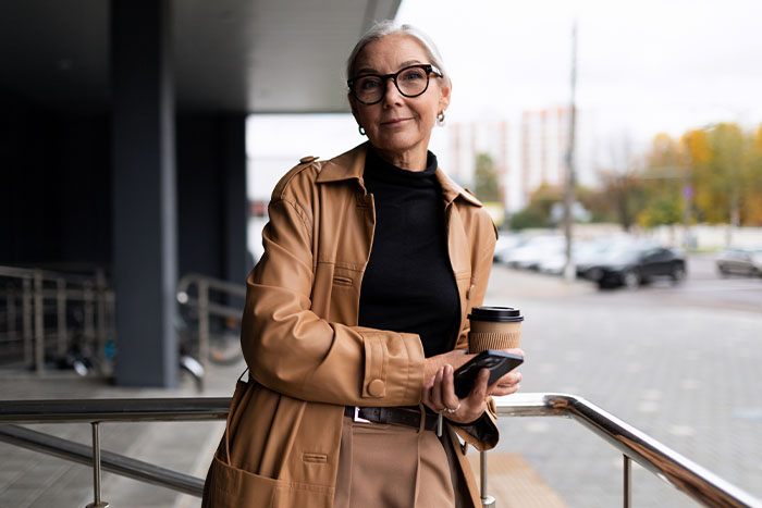 a businesswoman holding coffee and her phone smiles at the camera after exploring Gate City Bank’s enhanced digital banking