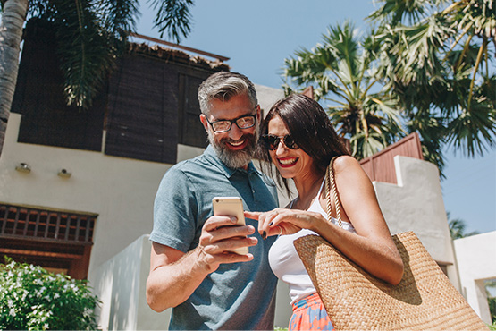 happy couple stands near vacation home and looks at a phone after learning tips for buying a second home from Gate City Bank