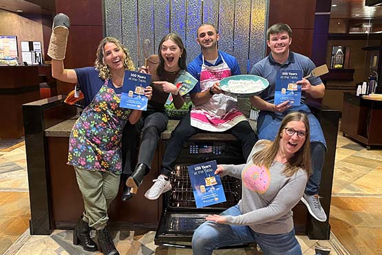 Lezan Tahir and his Fargo Gate City Bank team dress up as bakers and hold copies of the bank’s 100<sup>th</sup> anniversary cookbook