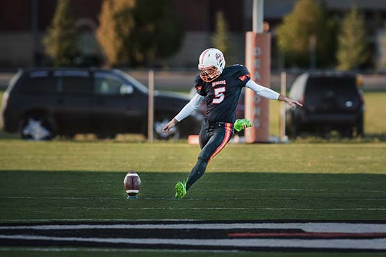 Wearing American football gear, Lezan Tahir runs to kick a ball outdoors while playing for the Fargo Invaders