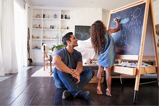 a happy father watches his young daughter draw new home plans on a chalkboard in their newly constructed home