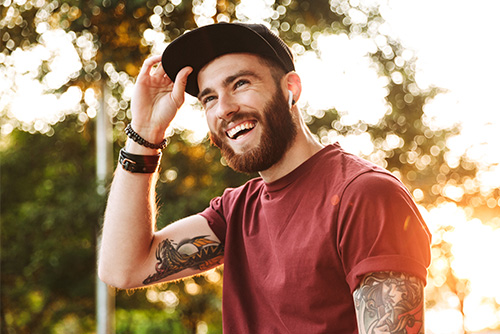 Young man with tattoos and beard, adjusting his baseball cap after walking out of Gate City Bank in Grand Forks