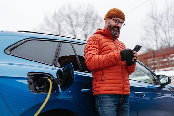 happy man leans on car during winter after reading Gate City Bank’s article on the reasons to buy an electric car or hybrid