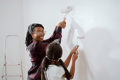 Image alt. text: Smiling mom and her daughter holding foam rollers, painting a white room while remodeling their home in Fargo, ND