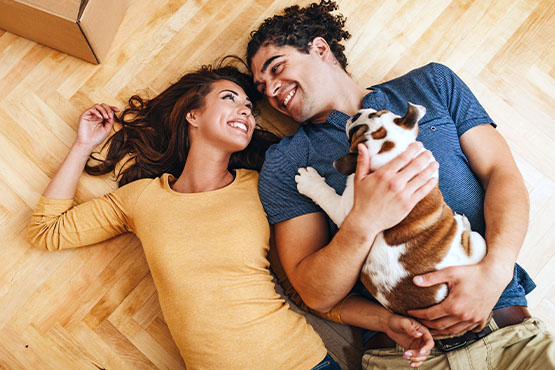 young woman smiling at her husband and bulldog puppy as they relax on the hardwood floor of their new home in Fargo, ND