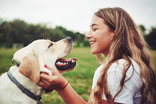 Teen girl with wavy hair, a local Gate City Bank checking customer in Fargo, ND, smiling at her golden Labrador retriever