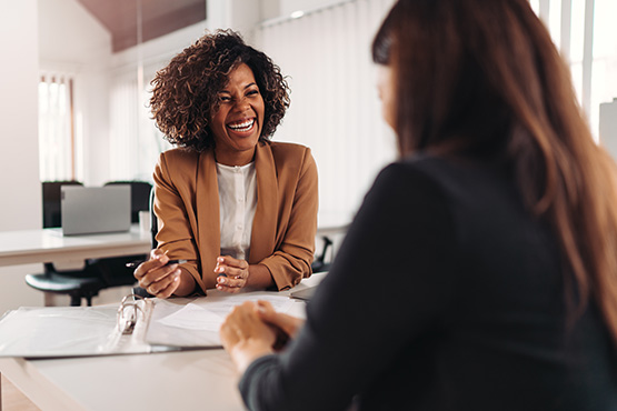 Friendly advisor in a tan blazer, laughing and talking with a client at her desk at Gate City Investment Services