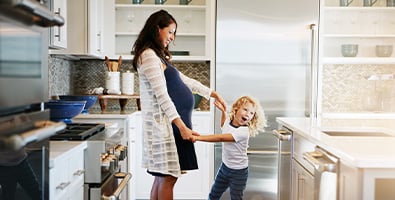 Laughing expecting mother and her daughter, twirling around together in the kitchen of their new Minnesota home