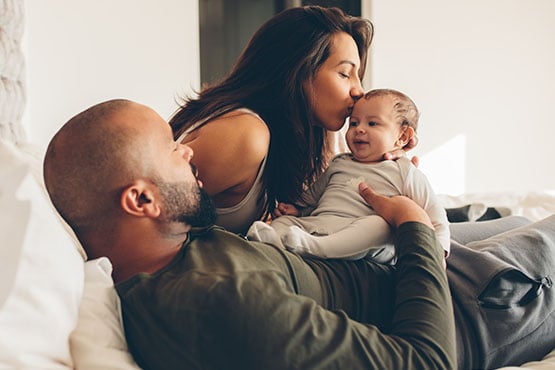 mom kissing newborn baby on the forehead, snuggled beside her husband in their new Fargo home