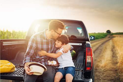 Farmer in a wheat field outside Carrington, ND, eating lunch in the bed of his pick-up with his young son