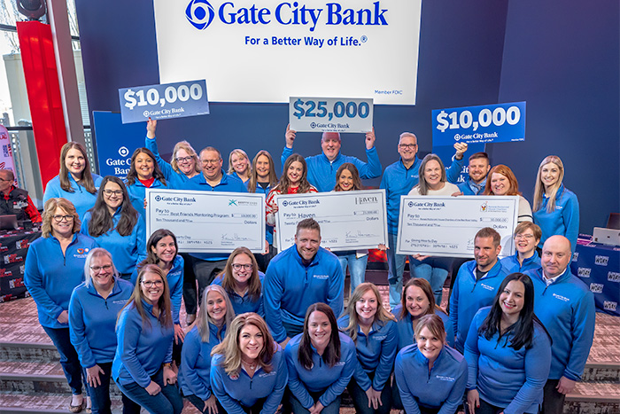 Gate City Bank team members with matching blue shirts pose for a pic with Giving Hearts Day charities and three giant checks