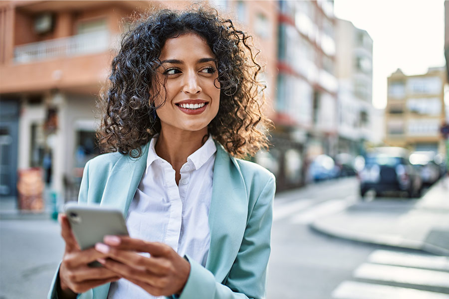 Curly-haired businesswoman in downtown Fargo, ND, smiling while reviewing transactions in her Gate City Bank mobile app