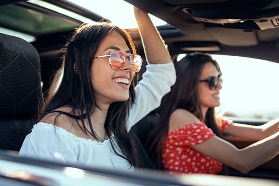 Two young women wearing sunglasses in Fargo, ND, driving their new car thanks to a Gate City Bank auto loan