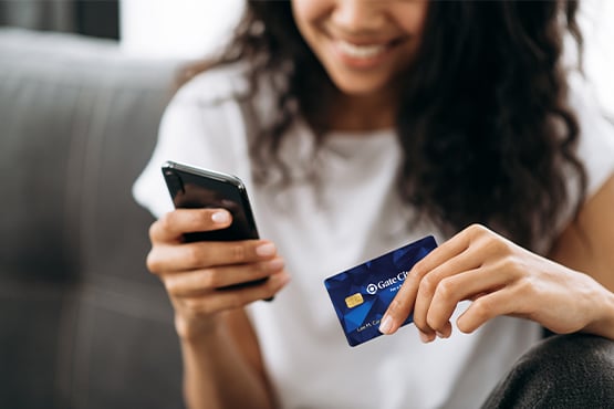 Close-up view of young brunette holding her Gate City Bank debit card while shopping on her phone during Amazon Prime Days