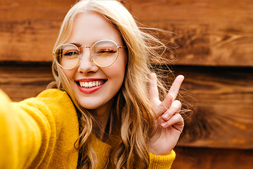 Smiling blonde woman in a gold sweater, making a peace sign on her way to open a new checking account in Mayville, ND.