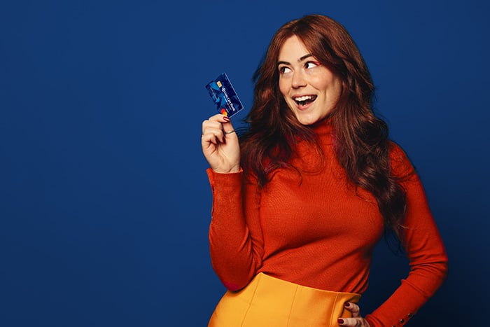 Smiling redhead in a red turtleneck, holding up her Gate City bank debit card after opening a Preferred Perks Checking account in downtown Fargo