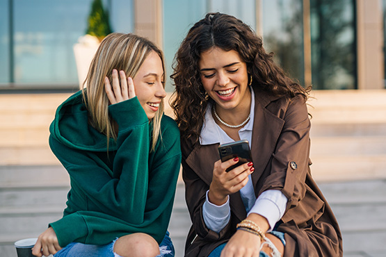 A young woman shows her friend the Gate City Bank app spending tool while sitting on her front porch steps in Fargo, ND