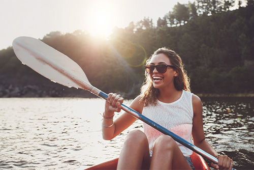 Laughing brunette in sunglasses, paddling her kayak across Pebble Lake in Fergus Falls, Minnesota