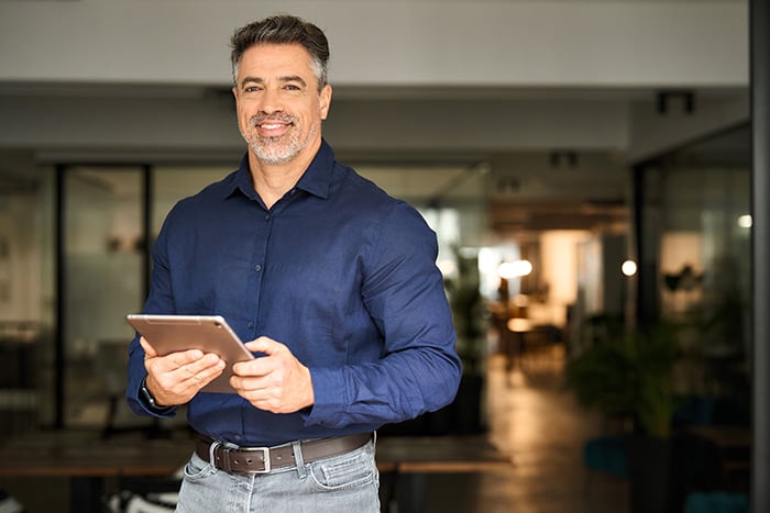 Silver-haired businessman in Grand Forks, ND, smiling while managing ACH origination and payment processing on his company tablet