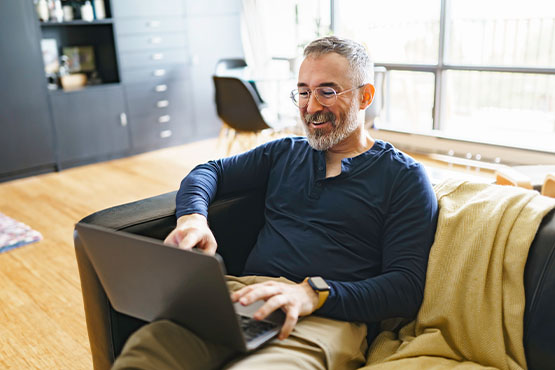 a smiling man uses a laptop to monitor his online banking accounts after reading Gate City Bank’s tips to prevent check fraud