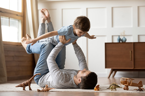 happy father lifting son into the air, playing airplane in the living room after personalizing his life insurance policy 