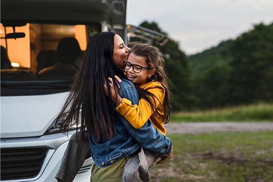 a happy mother holds her young daughter in front of a motorhome after reading Gate City Bank’s tips for buying an RV