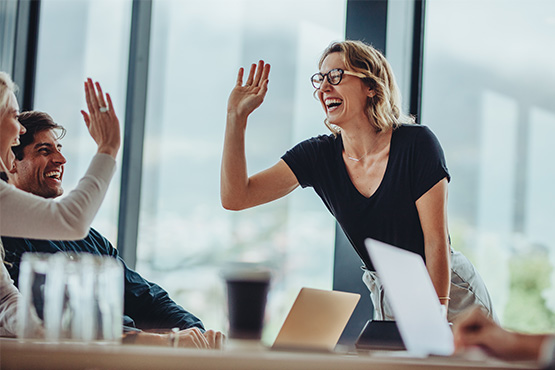 happy co-workers go in for a high five after learning about five business benefits of investing in employee retirement plans