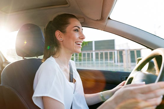 happy young woman in a white shirt drives around after learning tips for buying a car with bad credit and improving her score