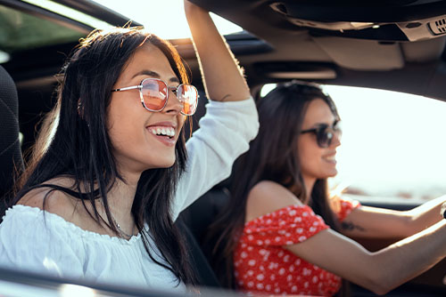 Two young women wearing sunglasses in Fargo, ND, driving their new car thanks to a Gate City Bank auto loan
