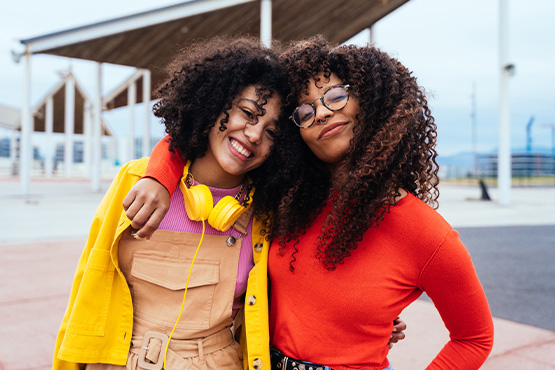 two happy young women share a side hug after reading Gate City Investment Services’ tips for retirement planning in your 20s