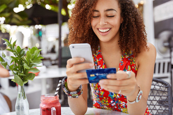 Young woman in a red halter top, smiling while holding a Gate City Bank debit card and checking her uChoose Rewards balance