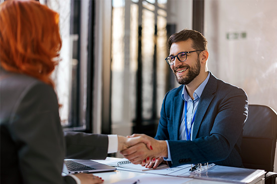 happy man wearing a professional suit shakes hands with a woman from across his desk after securing business retirement plans