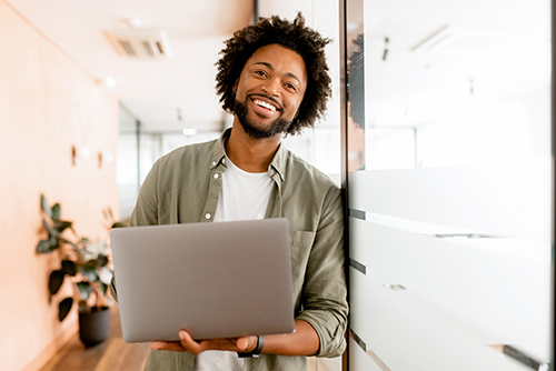 Cheerful young man with a beard, smiling after setting up a checking reserve line of credit on his laptop