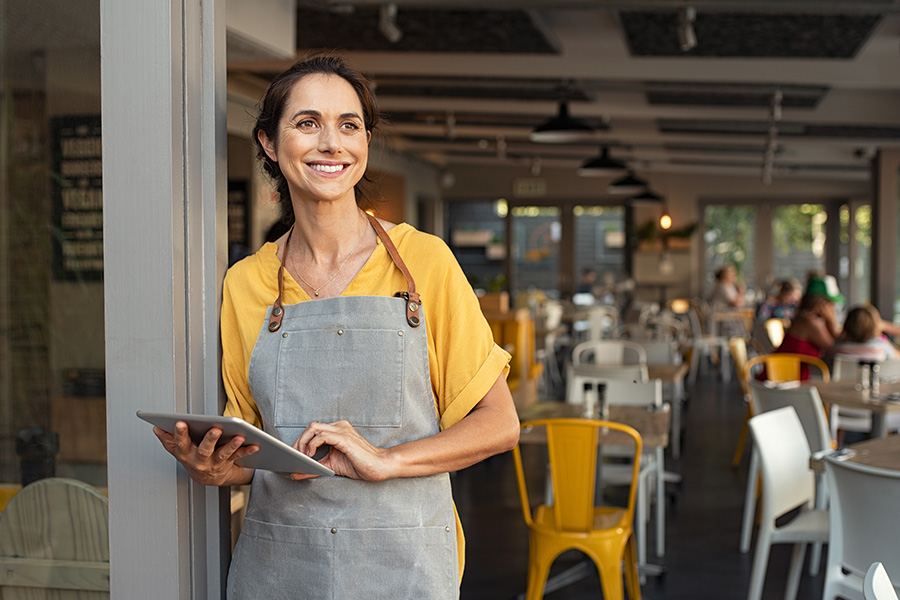 happy female cafe owner holds tablet used for business checking